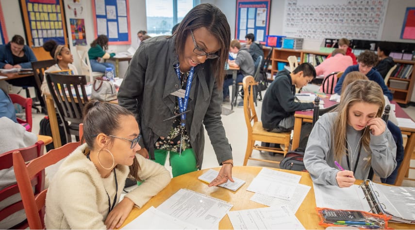 Female Clemson student-teacher answers one of her student's questions in a class full of students working independently.