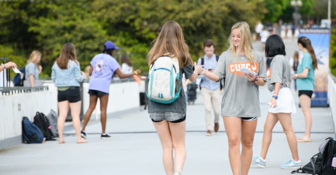 Female students hand out flyers on library bridge.