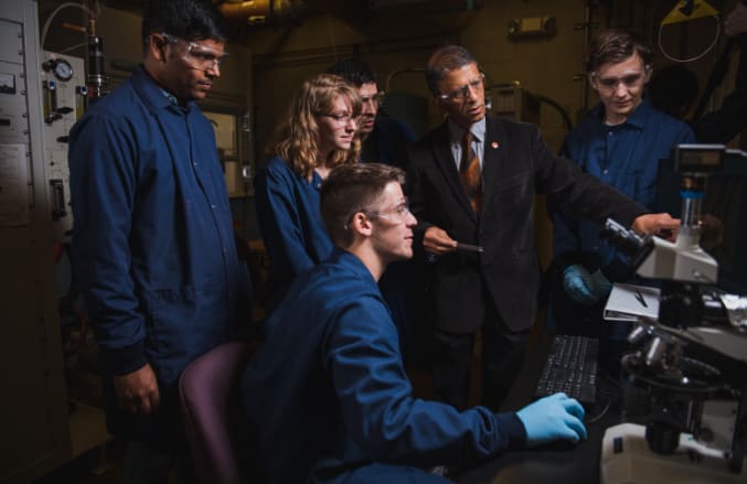 A team of graduate students and their professor examine a specimen with a microscope in the lab.