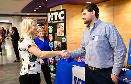 A female student and company representative, both wearing business casual clothing, shake hands at a career fair in Littlejohn Coliseum.