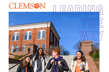 A group of four students laughs and talks while walking down a flight of stairs outside of a brick building.