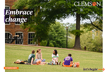 A student is studying on a grassy field in front of a tree and an old brick building.